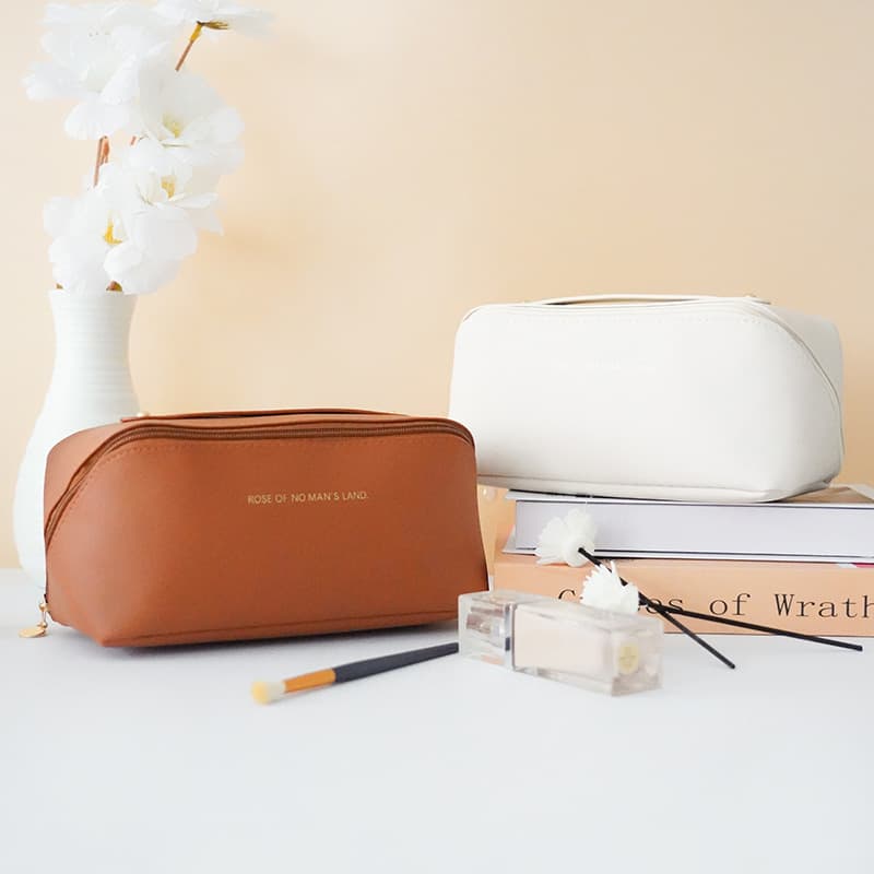Two leather cosmetic bags in brown and white, styled with flowers and makeup accessories.