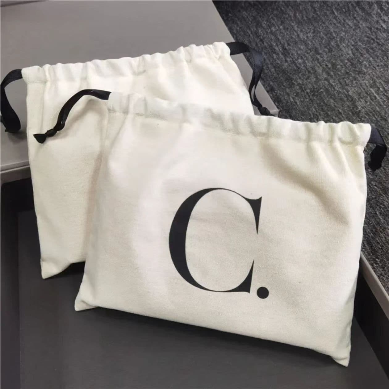 Two off-white drawstring dust bags with black ties, one featuring a large black letter C.