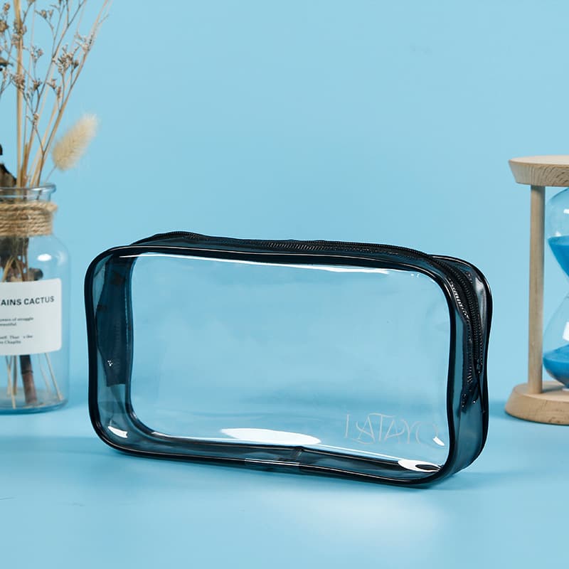 Clear rectangular toiletry bag with black trim and zipper on a light blue background.