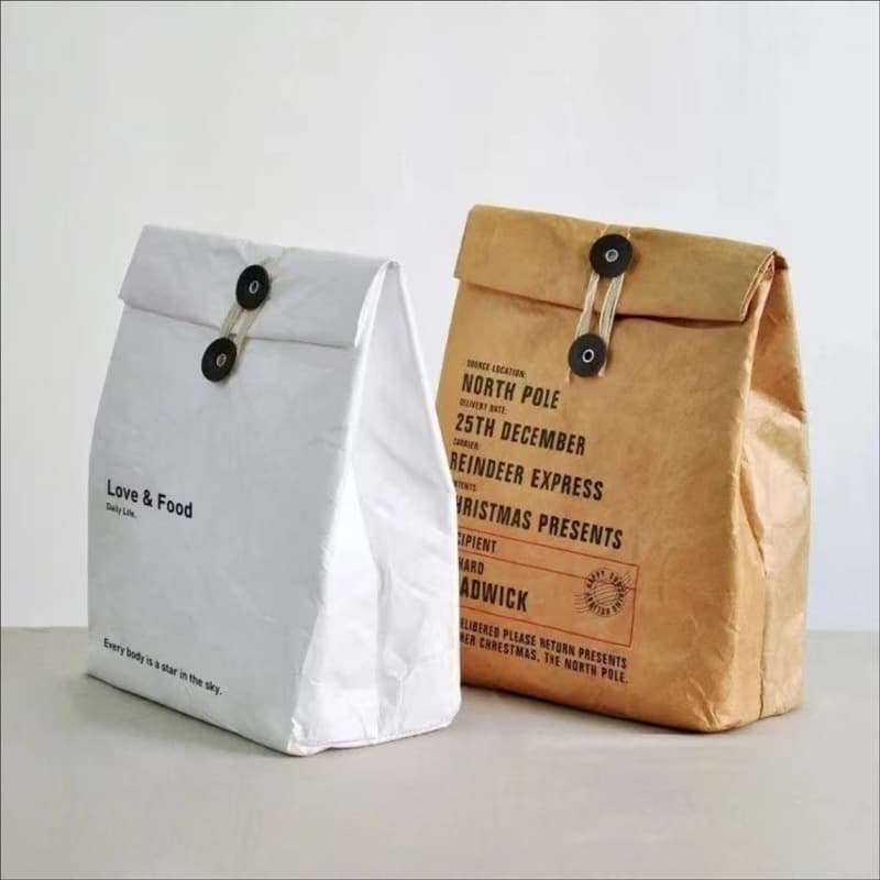 Reusable white and brown Tyvek lunch bags featuring button-and-string closures and decorative printed text.