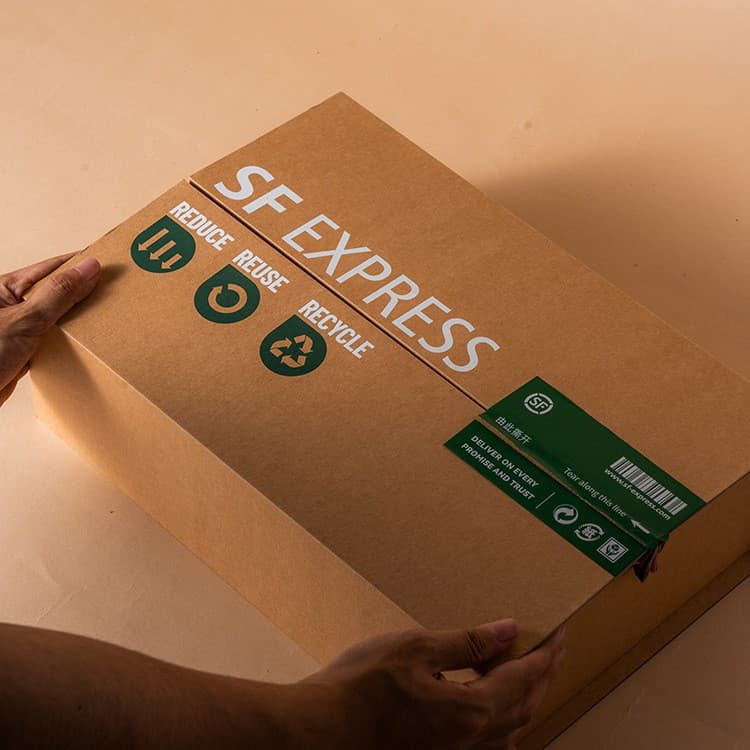 Hands holding an SF Express cardboard box with green reduce, reuse, and recycle icons.